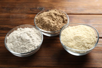 Photo of Different types of flour in bowls on wooden table, closeup