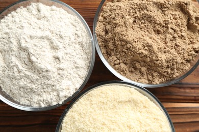 Photo of Different types of flour in bowls on wooden table, top view