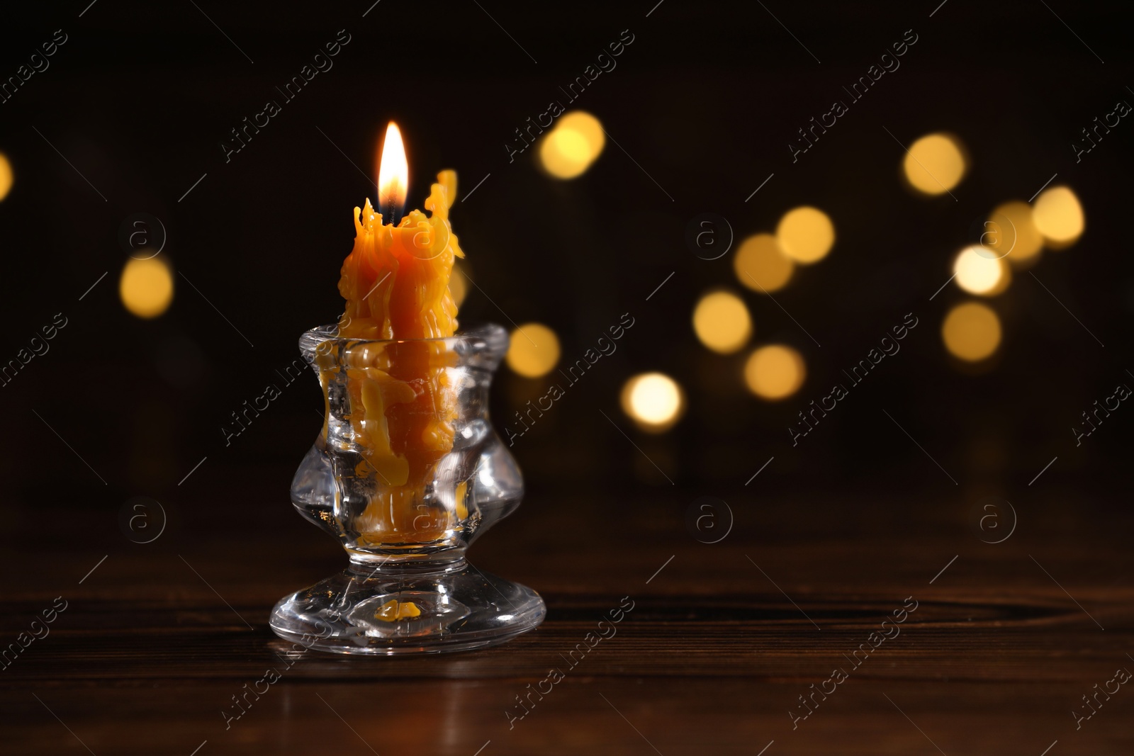 Burning candle in candlestick on wooden table against dark background with blurred lights, space for text. Bokeh effect Photo of Burning candle in candlestick on wooden table against dark background with blurred lights, space for text. Bokeh effect