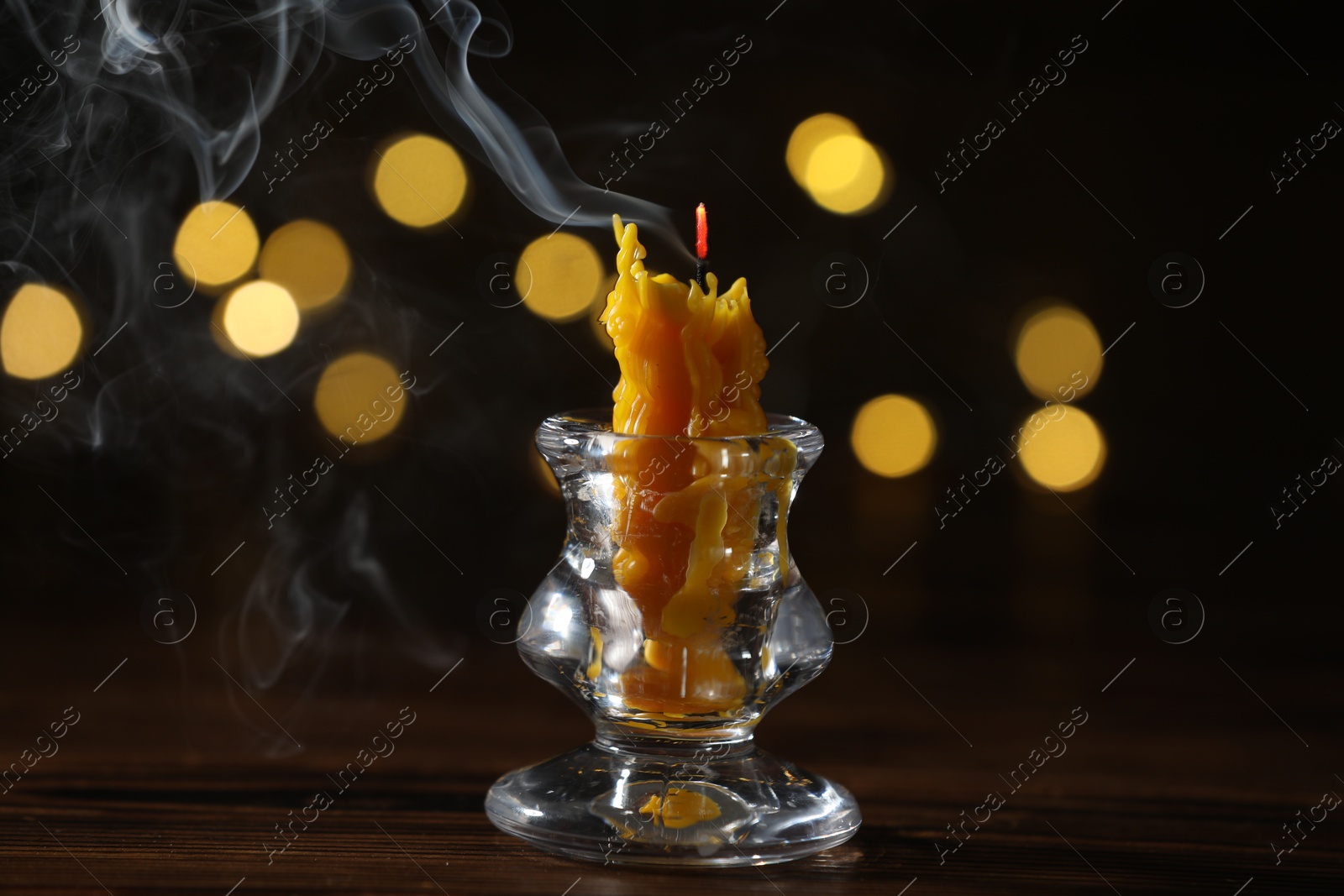 Extinguished candle in candlestick on wooden table against dark background with blurred lights. Bokeh effect Photo of Extinguished candle in candlestick on wooden table against dark background with blurred lights. Bokeh effect