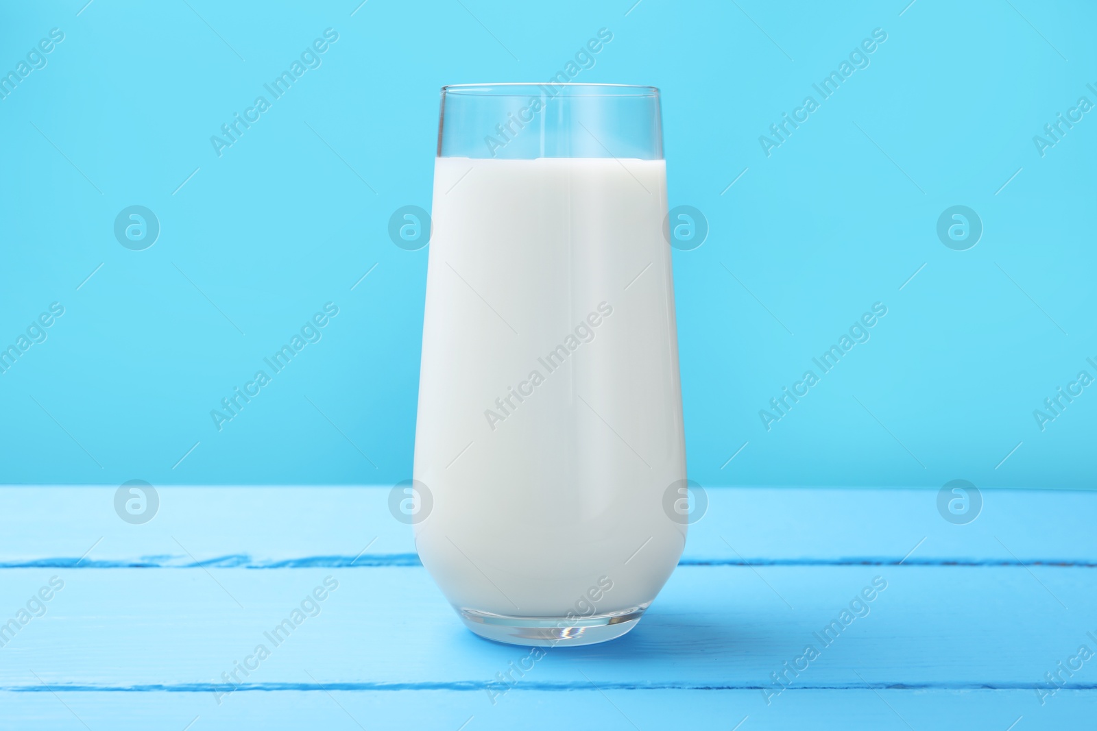 Fresh milk in glass on light blue wooden table Photo of Fresh milk in glass on light blue wooden table