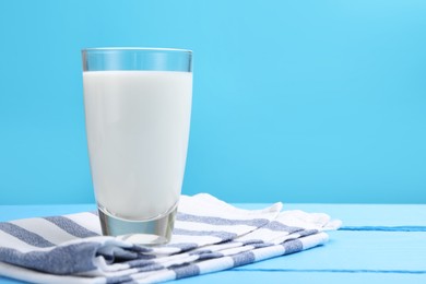 Photo of Fresh milk in glass on light blue wooden table. Space for text
