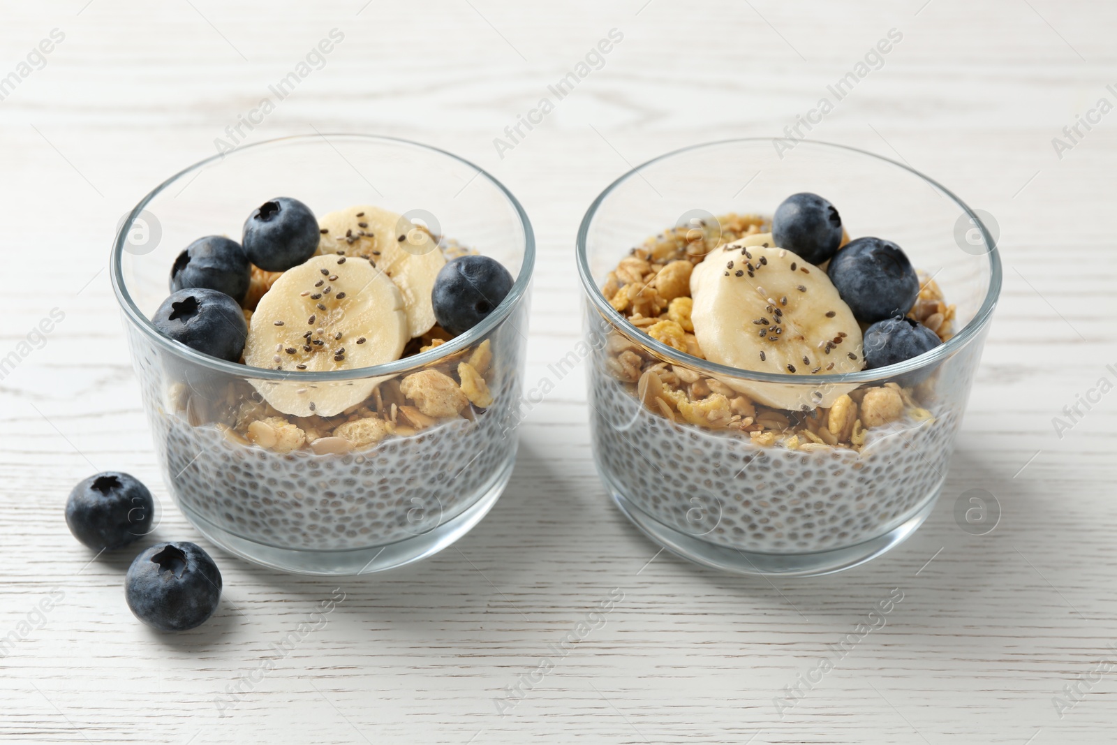 Delicious dessert with chia seeds, yogurt, granola, blueberries and banana on white wooden table, closeup. Superfood Photo of Delicious dessert with chia seeds, yogurt, granola, blueberries and banana on white wooden table, closeup. Superfood
