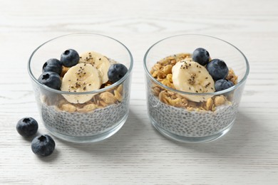 Photo of Delicious dessert with chia seeds, yogurt, granola, blueberries and banana on white wooden table, closeup. Superfood