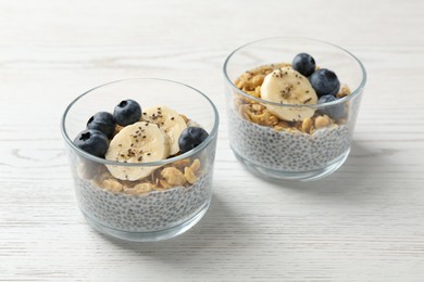 Photo of Delicious dessert with chia seeds, yogurt, granola, blueberries and banana on white wooden table, closeup. Superfood