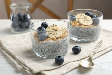 Photo of Delicious dessert with chia seeds, yogurt, granola, blueberries and banana on white wooden table, closeup. Superfood