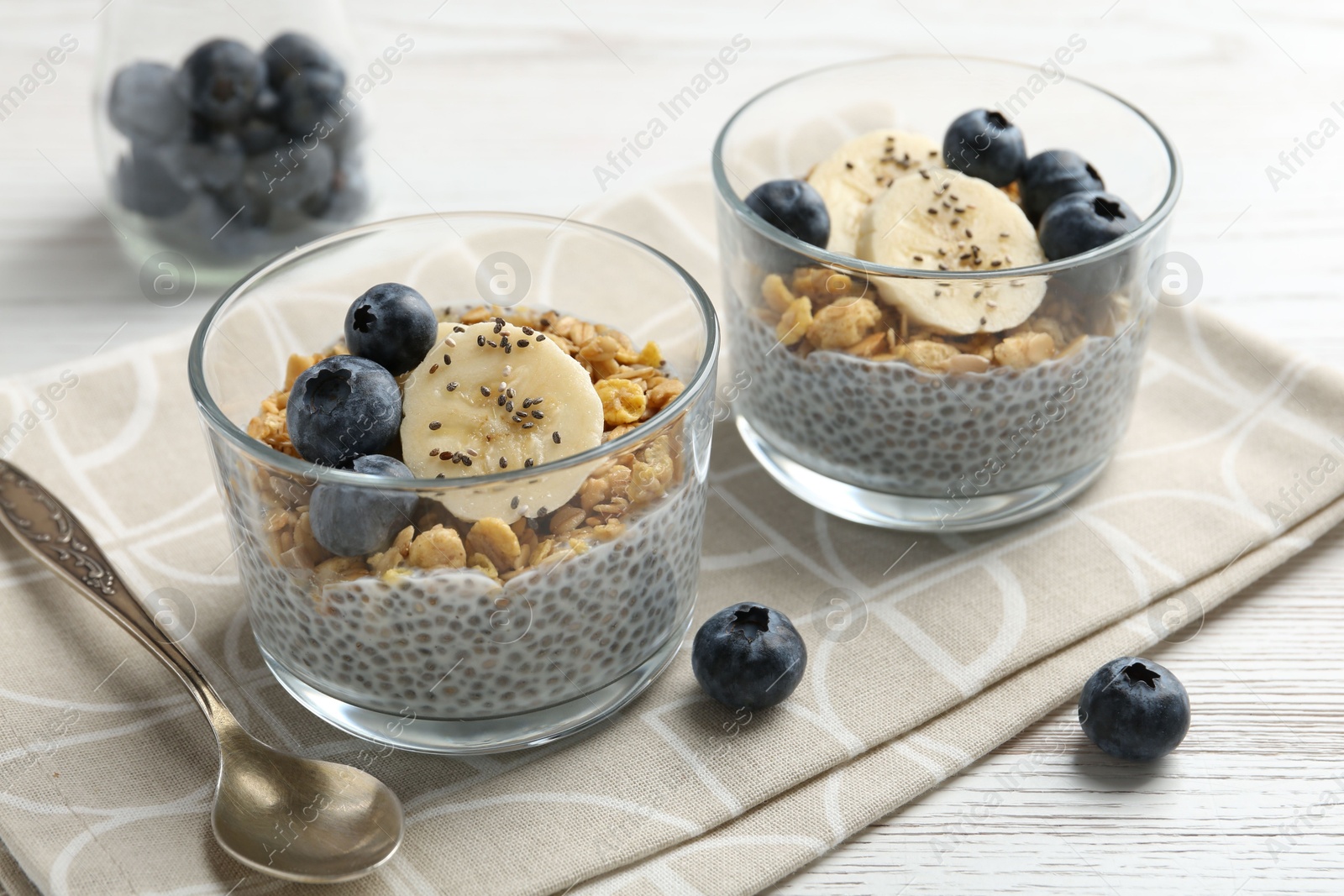 Delicious dessert with chia seeds, yogurt, granola, blueberries and banana on white wooden table, closeup. Superfood Photo of Delicious dessert with chia seeds, yogurt, granola, blueberries and banana on white wooden table, closeup. Superfood