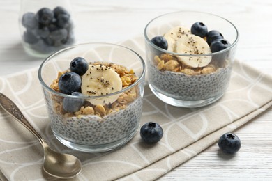 Photo of Delicious dessert with chia seeds, yogurt, granola, blueberries and banana on white wooden table, closeup. Superfood