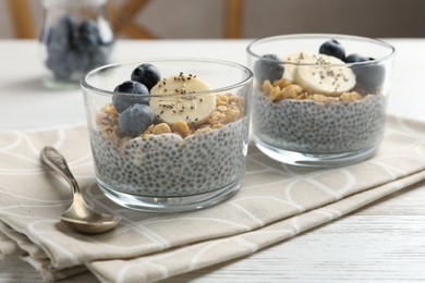 Photo of Delicious dessert with chia seeds, yogurt, granola, blueberries and banana on white wooden table, closeup. Superfood
