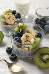 Photo of Delicious dessert with chia seeds, yogurt, granola, blueberries, banana and kiwi on white wooden table, closeup. Superfood