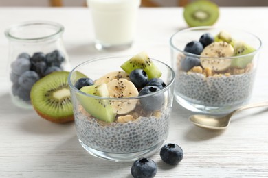 Photo of Delicious dessert with chia seeds, yogurt, granola, blueberries, banana and kiwi on white wooden table, closeup. Superfood