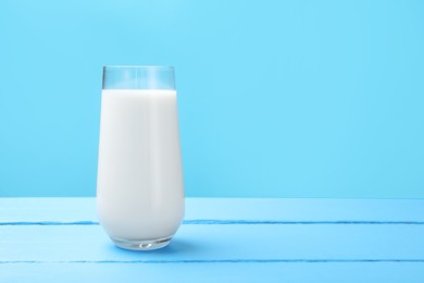 Photo of Fresh milk in glass on light blue wooden table. Space for text
