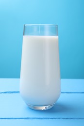 Photo of Fresh milk in glass on light blue wooden table, closeup