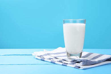 Photo of Fresh milk in glass on light blue wooden table. Space for text