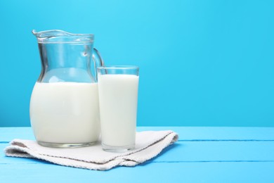 Photo of Fresh milk in glass and jug on light blue wooden table. Space for text