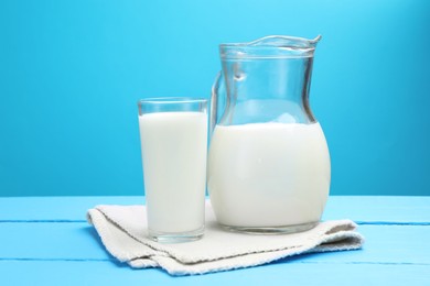 Photo of Fresh milk in glass and jug on light blue wooden table