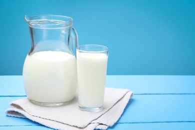 Photo of Fresh milk in glass and jug on light blue wooden table. Space for text