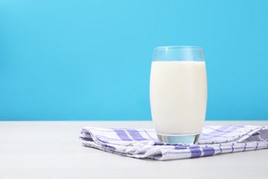 Photo of Fresh milk in glass on white wooden table against light blue background. Space for text