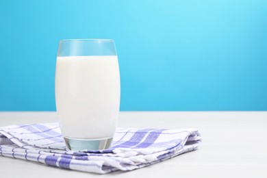 Photo of Fresh milk in glass on white wooden table against light blue background. Space for text