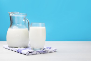 Photo of Fresh milk in glass and jug on white wooden table against light blue background. Space for text