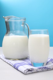 Fresh milk in glass and jug on white wooden table against light blue background