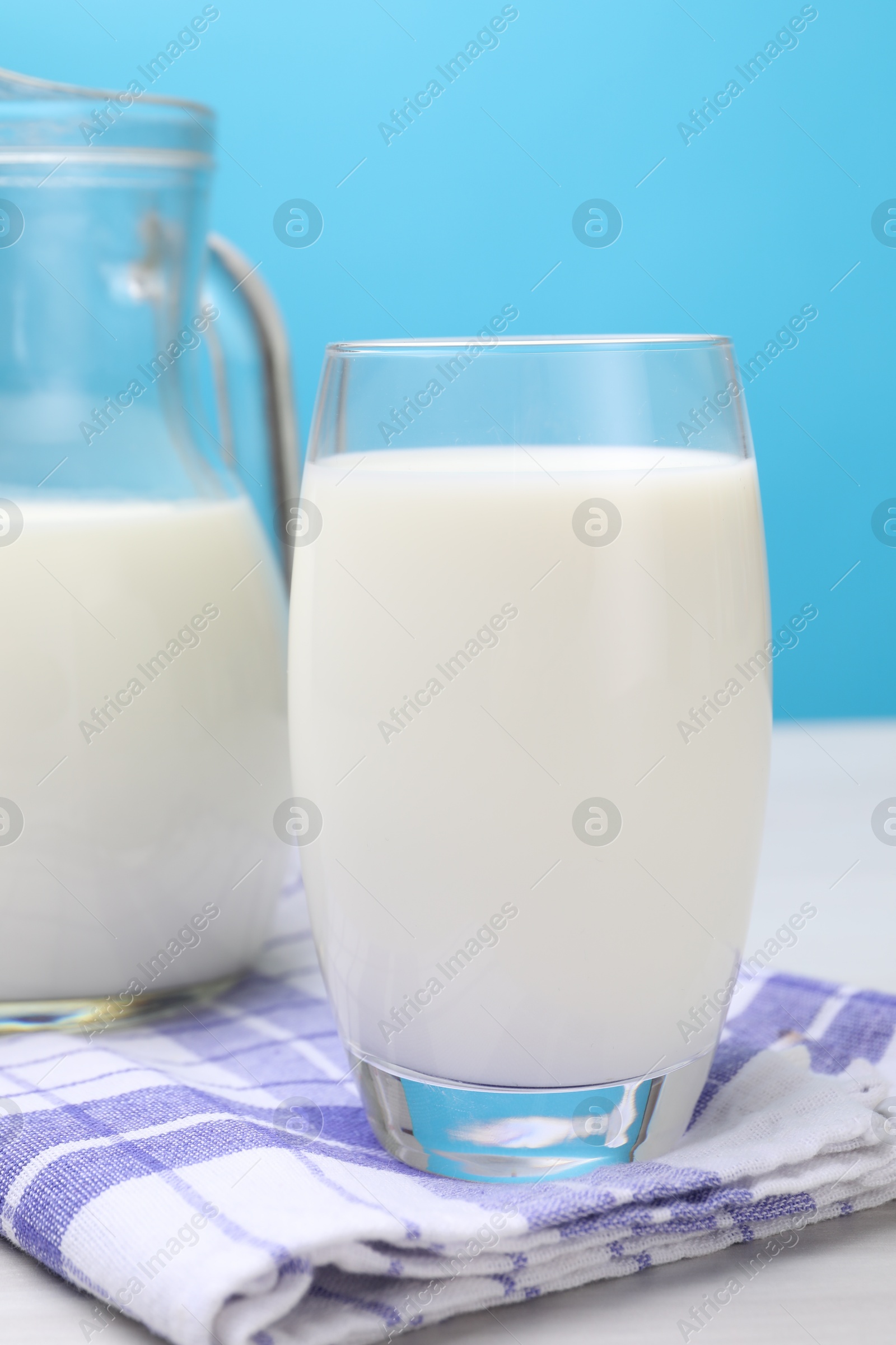Fresh milk in glass and jug on white wooden table against light blue background, closeup Photo of Fresh milk in glass and jug on white wooden table against light blue background, closeup