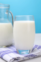 Photo of Fresh milk in glass and jug on white wooden table against light blue background, closeup