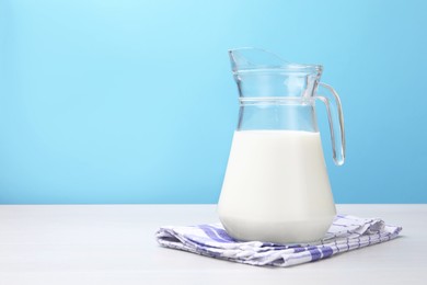Photo of Fresh milk in jug on white wooden table against light blue background. Space for text