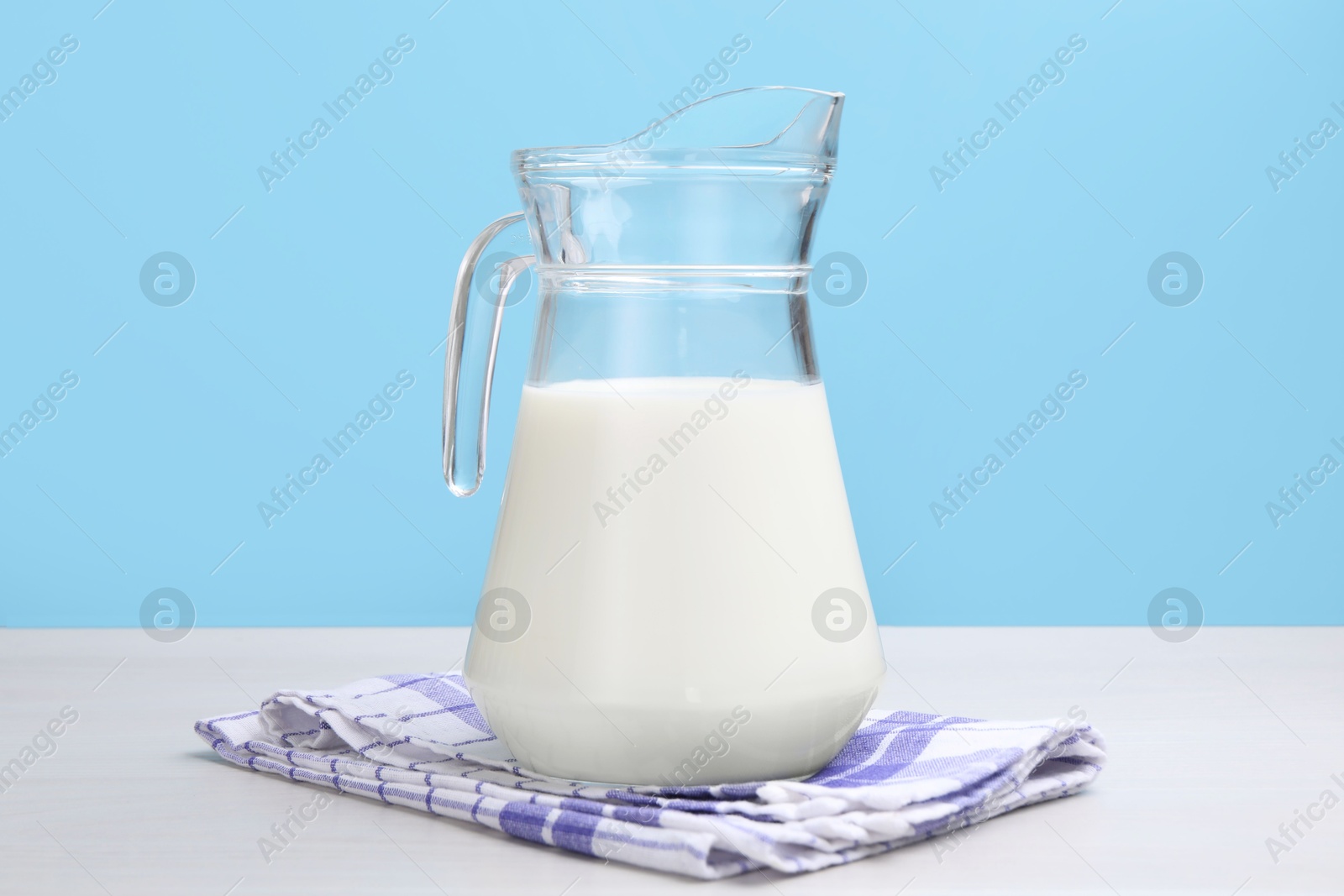 Fresh milk in jug on white wooden table against light blue background Photo of Fresh milk in jug on white wooden table against light blue background