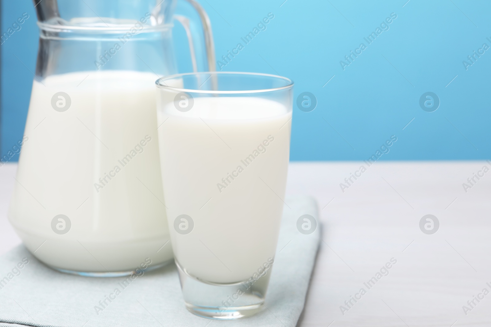 Fresh milk in glass and jug on white wooden table against light blue background, closeup. Space for text Photo of Fresh milk in glass and jug on white wooden table against light blue background, closeup. Space for text