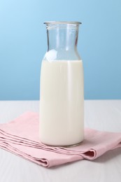 Photo of Fresh milk in jug on white wooden table against light blue background