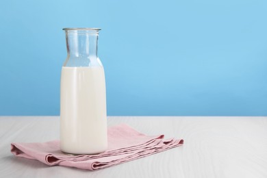Photo of Fresh milk in jug on white wooden table against light blue background. Space for text