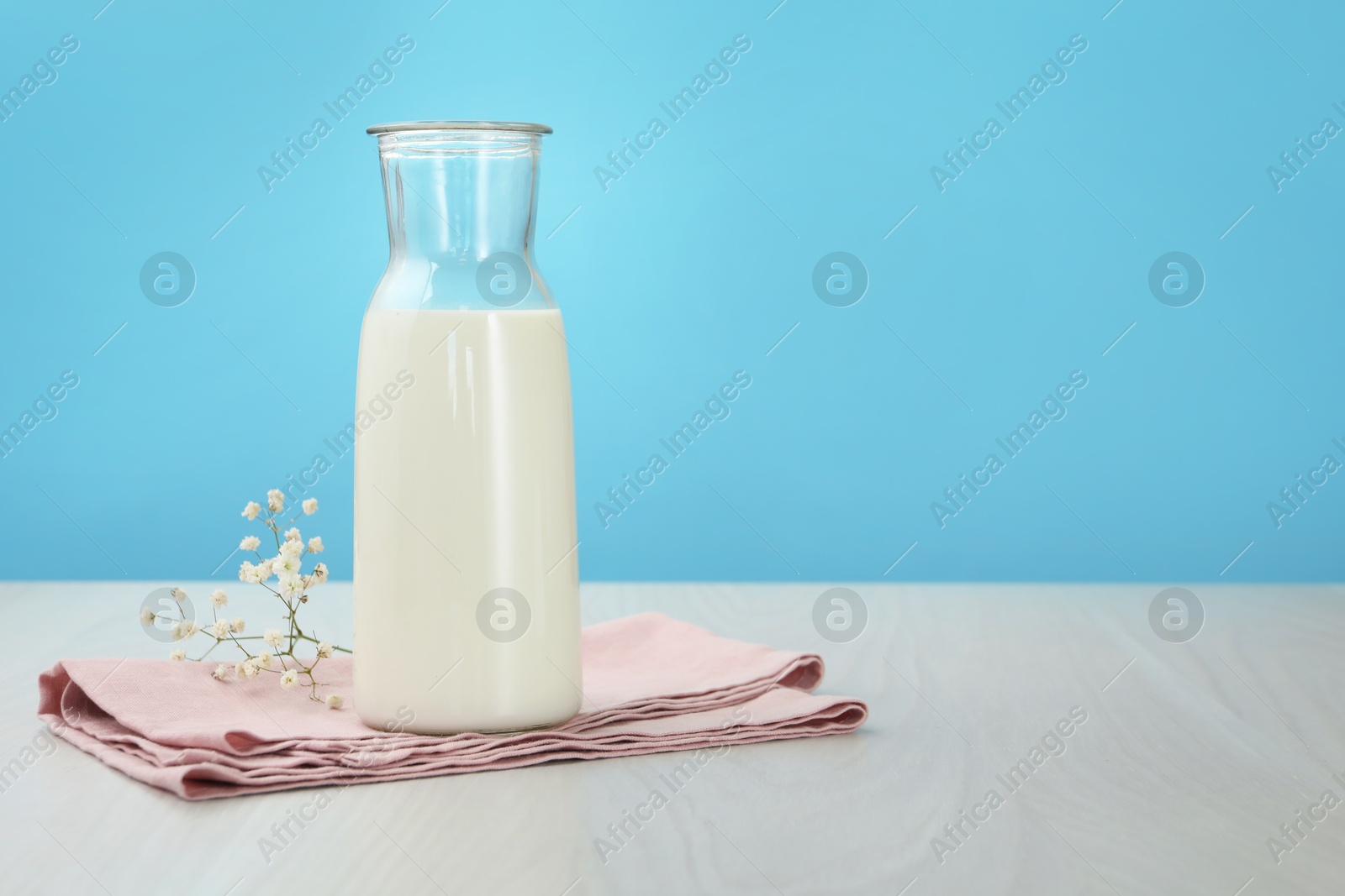 Fresh milk in jug and flowers on white wooden table against light blue background. Space for text Photo of Fresh milk in jug and flowers on white wooden table against light blue background. Space for text