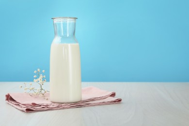 Photo of Fresh milk in jug and flowers on white wooden table against light blue background. Space for text