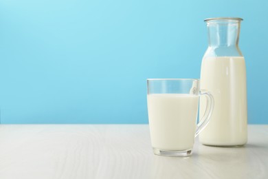 Photo of Fresh milk in cup and jug on white wooden table against light blue background. Space for text
