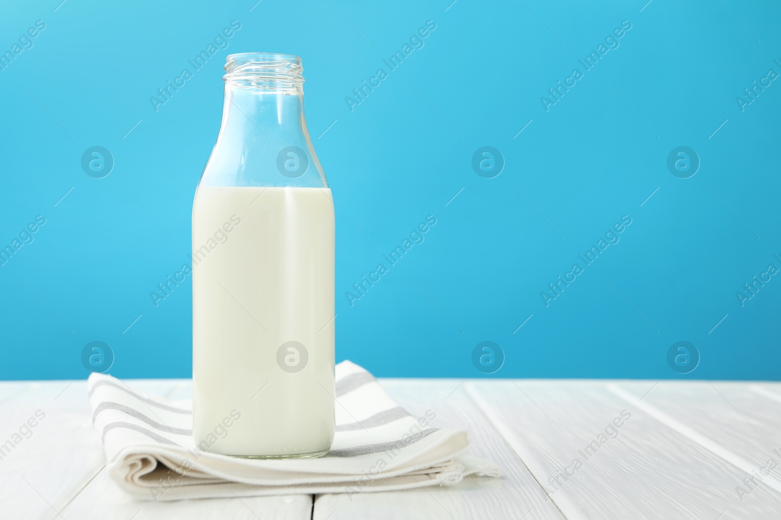 Fresh milk in glass bottle on white wooden table against light blue background. Space for text Photo of Fresh milk in glass bottle on white wooden table against light blue background. Space for text