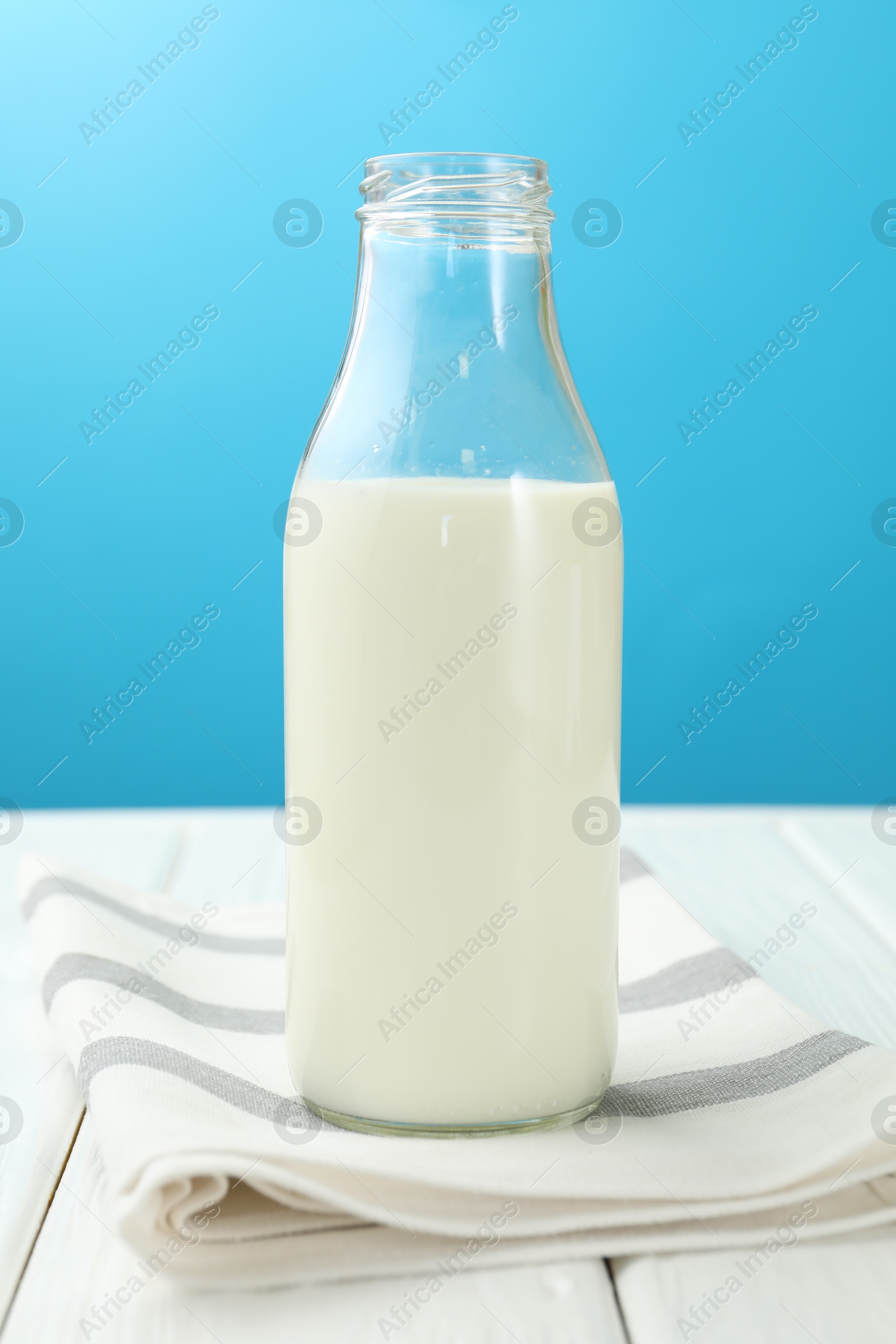 Fresh milk in glass bottle on white wooden table against light blue background Photo of Fresh milk in glass bottle on white wooden table against light blue background