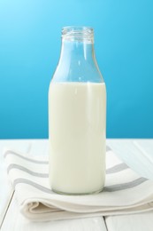 Photo of Fresh milk in glass bottle on white wooden table against light blue background