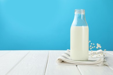 Photo of Fresh milk in glass bottle and flowers on white wooden table against light blue background. Space for text