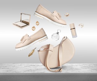 Image of Fashionable shoes, makeup products and accessories falling onto table against light grey background