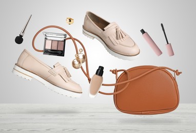 Image of Fashionable shoes, makeup products and accessories falling onto white wooden table against light grey background