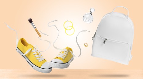 Image of Fashionable shoes and accessories falling onto table against beige background
