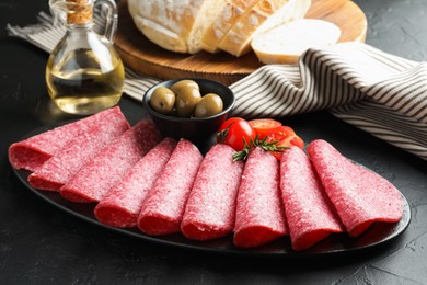Photo of Slices of delicious sausage with olives and tomatoes served on black table, closeup