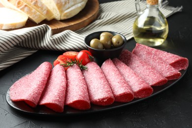 Photo of Slices of delicious sausage with olives and tomatoes served on black table, closeup