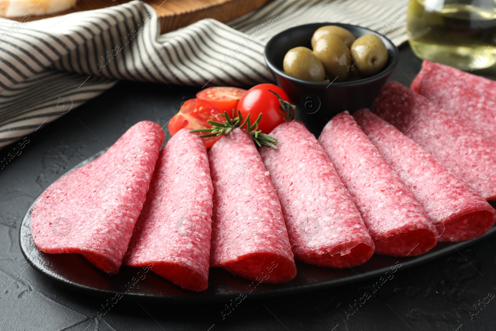 Slices of delicious sausage with olives and tomatoes served on black table, closeup Photo of Slices of delicious sausage with olives and tomatoes served on black table, closeup