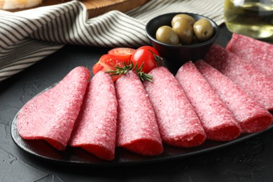 Photo of Slices of delicious sausage with olives and tomatoes served on black table, closeup