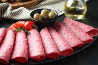 Photo of Slices of delicious sausage with olives and tomatoes served on black table, closeup
