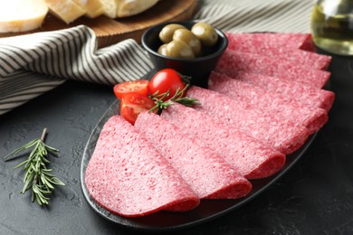 Photo of Slices of delicious sausage with olives and tomatoes served on black table, closeup