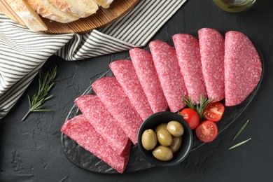 Photo of Slices of delicious sausage with olives and tomatoes served on black table, top view