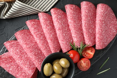 Photo of Slices of delicious sausage with olives and tomatoes served on black table, top view